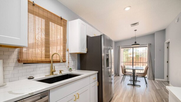 Una cocina moderna con armarios blancos, un refrigerador de acero inoxidable y un comedor con mesa y sillas.