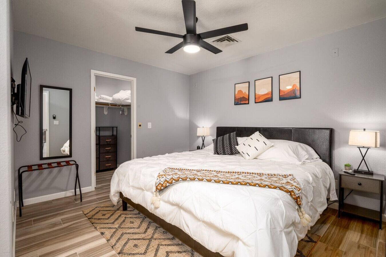 Ein Schlafzimmer mit einem Bett, einem Deckenventilator, einem Nachttisch, einer Lampe, einem Spiegel und einer Tür zu einem Kleiderschrank.