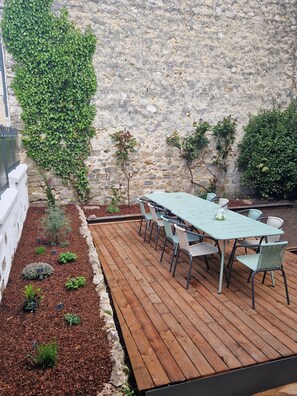 Eine Terrasse im Freien mit Holzdeck, einem Tisch mit Stühlen und einer mit Grünpflanzen bewachsenen Steinmauer.