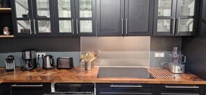 Una cocina con armarios oscuros, encimera de madera, cafetera, tostadora y hervidor.