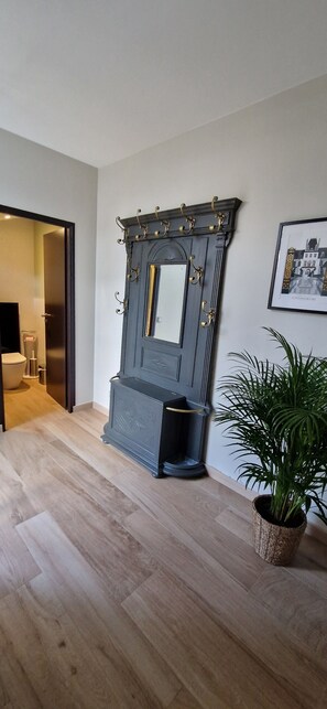 A room with a dark wooden cabinet with hooks, a framed mirror, and a potted plant.