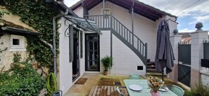 A patio area with a table and chairs, a potted plant, and a staircase leading to an upper level.