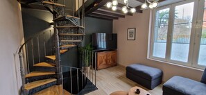 Un interior moderno con una escalera de caracol, un televisor de pantalla plana, un mueble de madera y un ventanal con vistas.