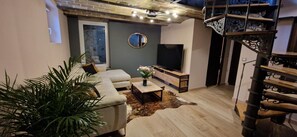 A living room with a sofa, coffee table, and a TV. There is a staircase with a decorative railing. - Bleautiful Joséphine - town house with garden (Fontainebleau)