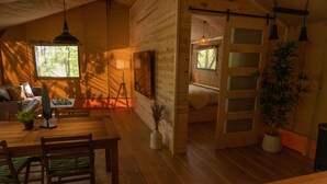 Een gezellig chaletinterieur met een houten eettafel, stoelen, een bank en een bed met een ladder.