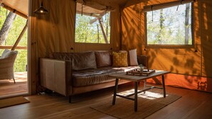 Een gezellige kamer met een leren bank, een houten salontafel en uitzicht op bomen door grote ramen.