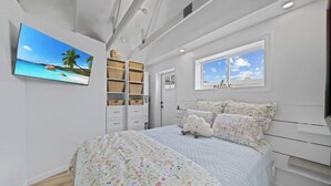 A bedroom with a bed, a TV mounted on the wall, a window with a view, and built-in shelves. - Charming Downtown Cottage w/ Modern Amenities (Coeur d'Alene)