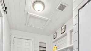 Un cuarto de lavandería con una puerta blanca, una lavadora, una secadora y un estante con una botella de detergente amarillo.