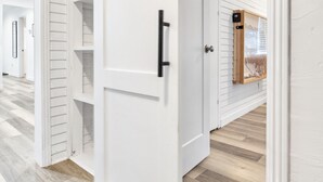 Una puerta corredera blanca con un pomo negro, que da paso a una habitación con paredes blancas empapeladas y suelo de madera.