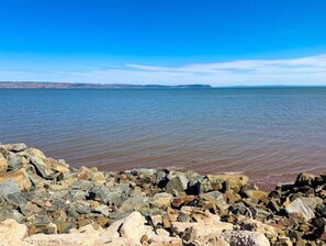 A rocky shoreline with a calm body of water and distant landforms. - Cottage at Evangeline Beach & near Local Wineries (Grand Pré)