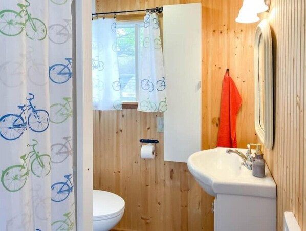 Ein Badezimmer mit Holzwänden, einer weißen Toilette, einem Waschbecken mit Spiegel und einem Duschvorhang mit Fahrradmotiven.