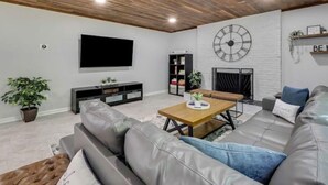 Een moderne woonkamer met een houten plafond, een grote wandklok, een flatscreen-tv, een open haard en een bank.