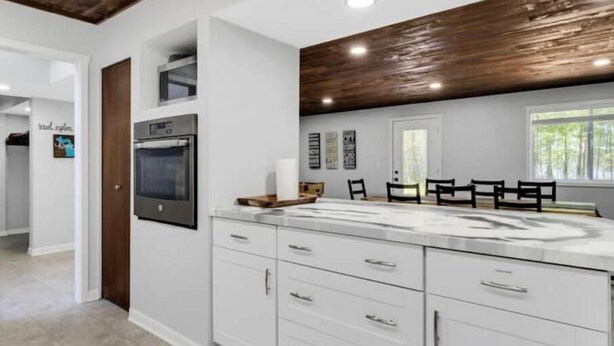 Een moderne keuken met witte kasten, een inbouwoven en een houten plafond.