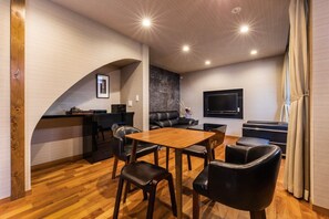 Una sala de estar moderna con una mesa de comedor de madera, sillas de cuero negro, un sofá de cuero negro y un televisor de pantalla plana montado en la pared.