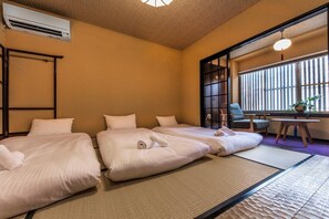 Habitación de hotel con dos camas, suelo de esteras de tatami, escritorio con silla y ventana grande con persianas.
