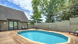 Um deck de madeira com piscina, móveis de exterior e um edifício com porta de correr de vidro.
