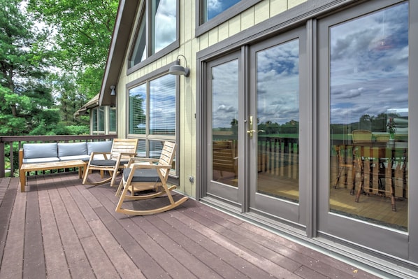A deck with outdoor furniture, including a sofa and rocking chairs, and a glass door leading to a patio area.