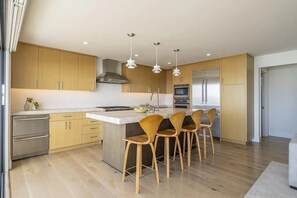 Cozinha moderna com armários de madeira, eletrodomésticos de aço inoxidável e uma ilha central com banquetas.