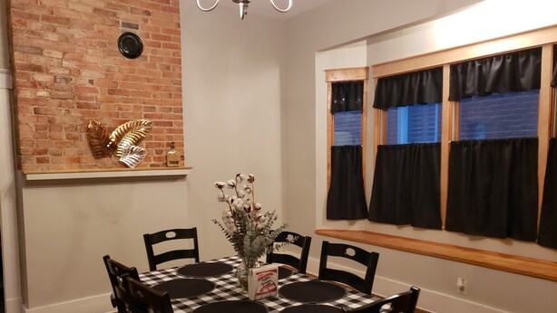 Un comedor con mantel a cuadros, sillas negras y un jarrón con flores.