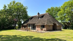 Une maison à toit de chaume, aux murs en briques, dotée d’un porche et d’une pelouse.