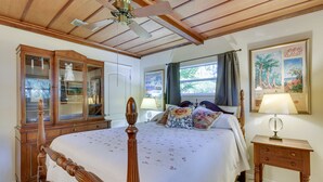 Een slaapkamer met een houten bed, nachtkastje, dressoir en plafondventilator.