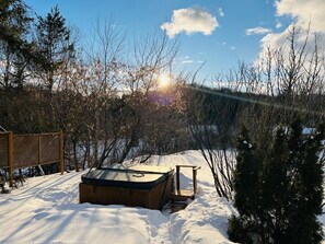Lämmin poreallas lumisessa ulkotilassa, jossa on puinen terassi ja näkymä puihin ja kukkulalle.