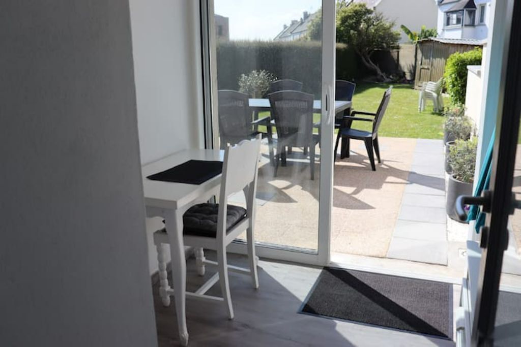 Eine Terrasse mit Tisch und Stühlen, eine Glasschiebetür, die zu einem Garten führt, und ein kleiner Podeststufenabgang zum Raum.