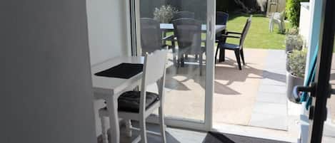 A patio area with a table and chairs, a sliding glass door leading to a garden, and a small step leading into the room.