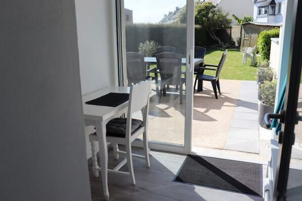 A patio area with a table and chairs, a sliding glass door leading to a garden, and a small step leading into the room.