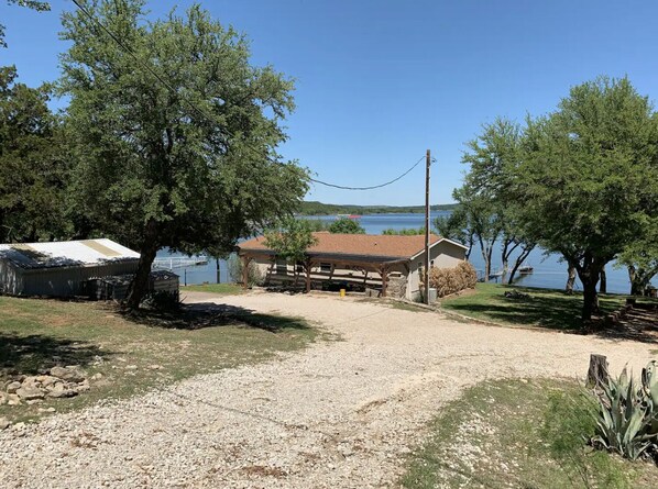 A rustic cabin with a gravel driveway leading to a wooden deck, surrounded by trees and overlooking a lake. - Peace on Possum Kingdom Lake- WATERFRONT with a large deck to escape and relax (Caddo)