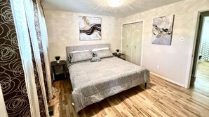 Une chambre à coucher comprenant un lit, deux tables de chevet, un luminaire au plafond et deux portes.