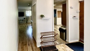 Un couloir avec un plancher en bois, un étagère en métal, une poubelle et un tapis bleu à l’entrée.