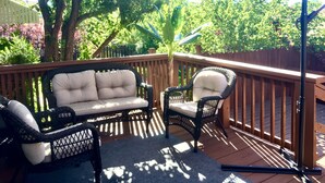 Une terrasse dotée de meubles en osier, notamment d’un canapé et de deux fauteuils, protégée par un grand parasol.