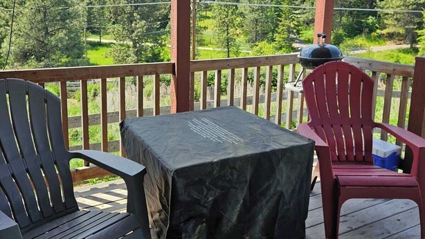 A covered outdoor area with a table and chairs, a grill, and a view of a forest. - Tiny Farmhouse | CDA, Silverwood & Lake Nearby (Coeur d'Alene)