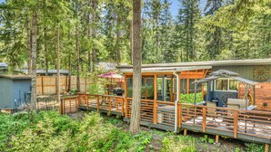 A wooden deck with outdoor seating, a barbecue area, and a covered section with a wheel. - Couples Retreat! Every Season-Luxury, River Front, Hot tub and outdoor Shower (Glide)