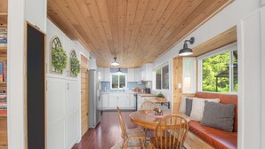 A cozy kitchen with wooden ceiling and white cabinets, a dining area with a round table and chairs, and a built-in bench with cushions. - Couples Retreat! Every Season-Luxury, River Front, Hot tub and outdoor Shower (Glide)