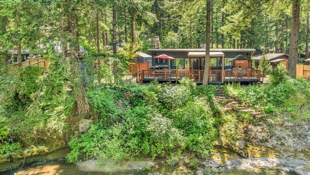 A cabin with a deck overlooking a forested area and a stream. - Couples Retreat! Every Season-Luxury, River Front, Hot tub and outdoor Shower (Glide)