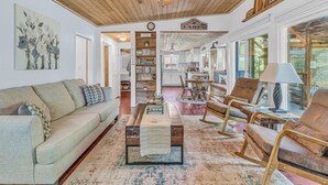 A spacious living room with a wooden ceiling, a sofa, a coffee table, and a bookshelf. - Couples Retreat! Every Season-Luxury, River Front, Hot tub and outdoor Shower (Glide)