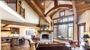 A spacious living area with a fireplace, wooden beams, a kitchen with a stone island, and large windows offering a view of the outdoors. - Beautiful, Comfortable, Well Appointed House; Amazing Views, Excellent Location (Park City)