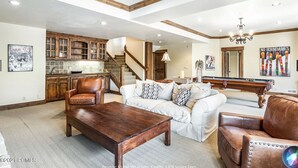 A spacious living room with a wooden coffee table, leather armchairs, and a white sofa. A pool table is visible in the background. - Beautiful, Comfortable, Well Appointed House; Amazing Views, Excellent Location (Park City)