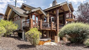 A two-story log cabin with a balcony, stone foundation, and a hot tub in the front yard. - Beautiful, Comfortable, Well Appointed House; Amazing Views, Excellent Location (Park City)