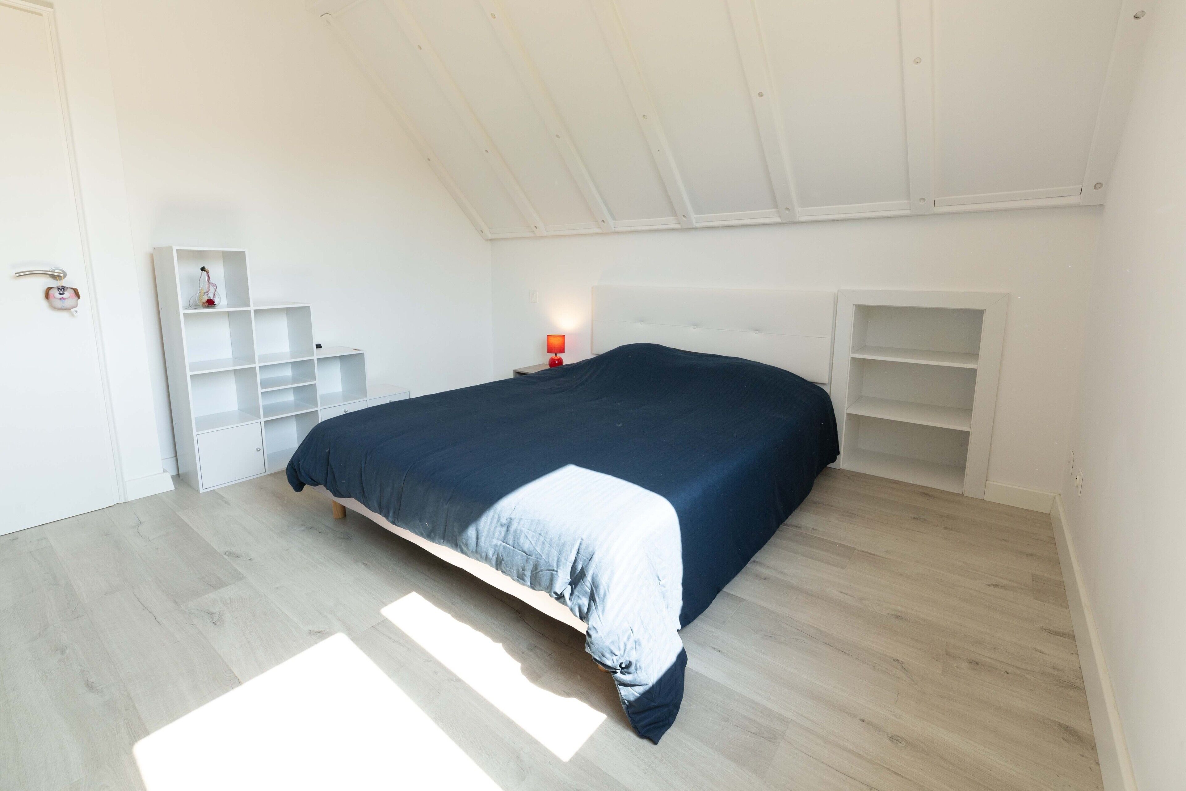 A bedroom with a bed, a nightstand, a shelf unit, and a wardrobe.