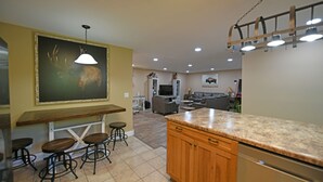 A kitchen with a wooden countertop, bar stools, and a large painting on the wall. - Two Homes in One! Bear Hollow is the Perfect Luxury Escape for Large Gatherings! (Sevierville)