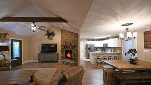 A spacious living room with a fireplace, a dining area, and a kitchen in the background. - Two Homes in One! Bear Hollow is the Perfect Luxury Escape for Large Gatherings! (Sevierville)