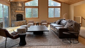 Un salón espacioso con chimenea de piedra, ventanas grandes y un techo alto de madera.