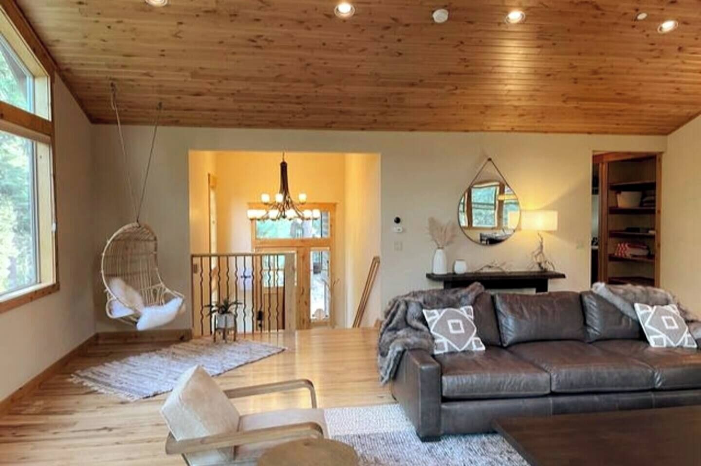 Un salón amplio con techo de madera, un sofá de cuero, una silla colgante y una escalera que conduce a un nivel superior.