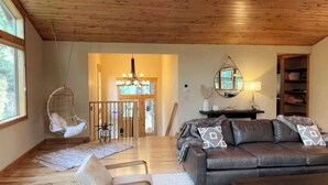 Un salón amplio con techo de madera, un sofá de cuero, una silla colgante y una escalera que conduce a un nivel superior.