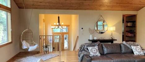 Un salón amplio con techo de madera, un sofá de cuero, una silla colgante y una escalera que conduce a un nivel superior.