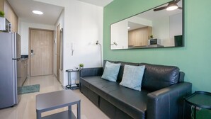 Een moderne woonkamer met een zwarte leren bank, een klein tafeltje, een groene wand en een grote spiegel.