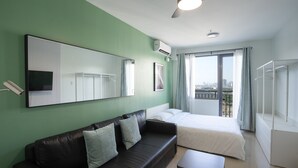 Een moderne hotelkamer met een groene wand, een zwarte leren bank, een enkel bed en een balkon met uitzicht op de stad.
